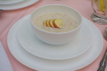 Oatmeal with apple for breakfast. Healthy eating. A useful breakfast. Porridge in a white ceramic cup on a pink tablecloth.