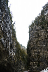 View from below of a mountain gorge with high cliffs and clouds, cloudy autumn day