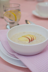 Oatmeal with apple for breakfast. Healthy eating. A useful breakfast. Porridge in a white ceramic cup on a pink tablecloth.