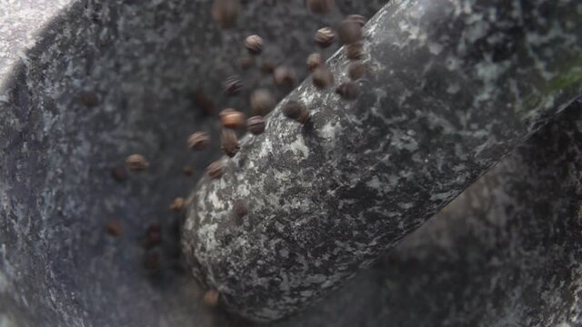Spicy black peppercorns are falling into the grey stone mortar in slow motion