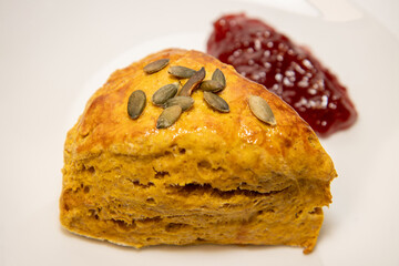A delicious plate of a pumpkin spice scone with jam on a white background plate