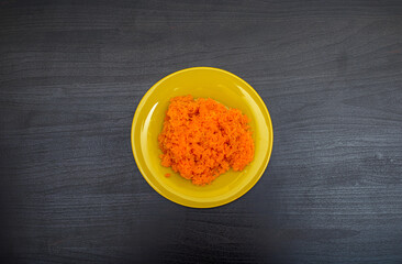 An ingredient for making various salads and snacks. Mashed boiled carrots in a yellow plate on a dark wooden table. Flat lay