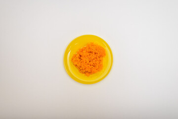 An ingredient for making various salads and snacks. Mashed boiled carrots in a yellow plate isolated on a white background. Flat lay