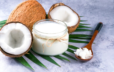 Coconut milk in glass bottle and fresh coconuts with half on a gray background