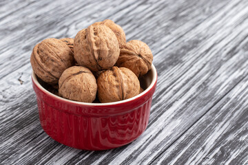 Whole walnuts in red bowl on black wooden background.
