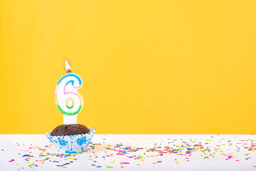 6 number candle on a cup cake with colorful sprinkles and yellow background sixth birthday...