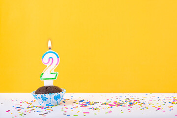 2 number candle on a cup cake with colorful sprinkles and yellow background second birthday anniversary celebrations