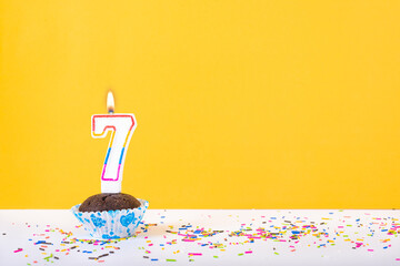 7 number candle on a cup cake with colorful sprinkles and yellow background seventh birthday anniversary celebrations