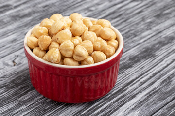 Peeled hazelnut on black wooden table. Hazelnut kernels in red bowl.