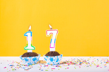 17 number candle on a cup cake with colorful sprinkles and yellow background seventeenth birthday...