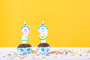29 number candle on a cup cake with colorful sprinkles and yellow background twenty ninth birthday...