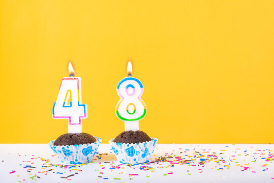 48 number candle on a cup cake with colorful sprinkles and yellow background forty eighth birthday anniversary celebrations