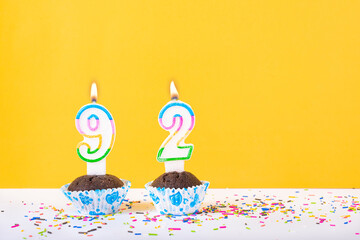 92 number candle on a cup cake with colorful sprinkles and yellow background ninety second birthday...