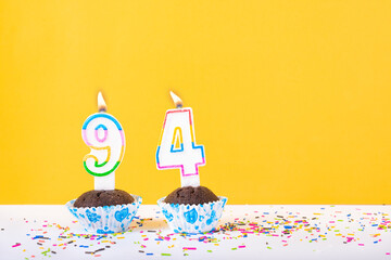 94 number candle on a cup cake with colorful sprinkles and yellow background ninety fourth birthday...