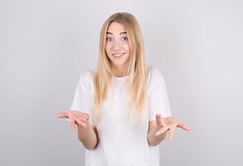 Portrait of attractive blonde woman wearing white shirt showing I don't know gesture isolated over grey background