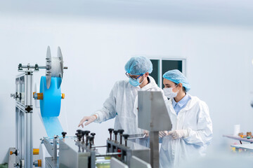 Naklejka premium Staff and workers at the mask factory are monitoring the operation of the machines. A mask is being produced on machine. Factory workers are discussing.