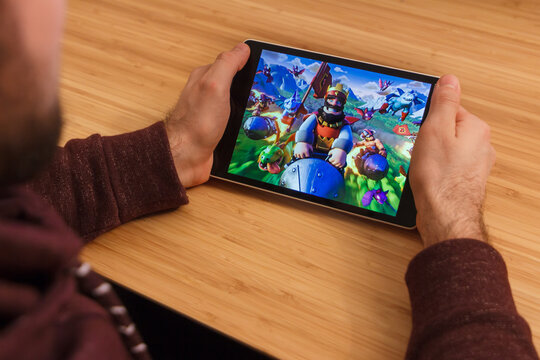 PRAGUE, CZECH REPUBLIC - MARCH 16, 2019: Man holding a smartphone and playng the Clash Royale mobile game. An illustrative editorial image on an bamboo background.
