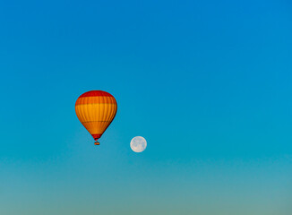 Hot air balloon flying over Cappadocia with full moon, in blue sky