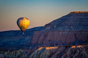 Hot air balloon flies between fairy chimneys and hills in Cappadocia, beautiful sun lights and magnificent view in the morning