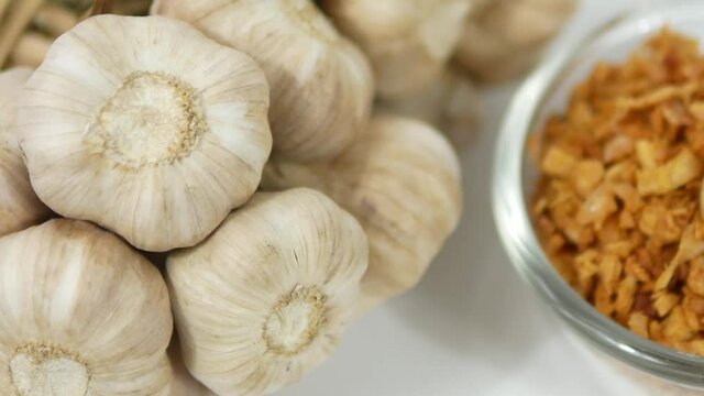 A bunch of fresh garlic and chopped fried garlic in bowl on white background