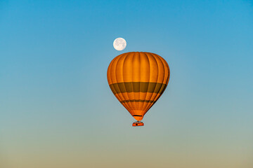 Hot air balloon flying over Cappadocia with full moon, in blue sky