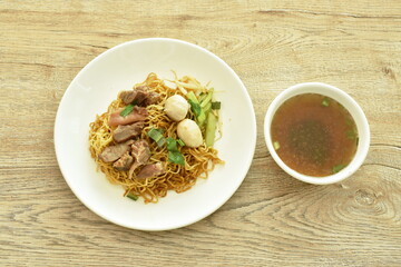 Chinese yellow egg noodles topping braised pork and ball on plate with bone in brown herb soup cup