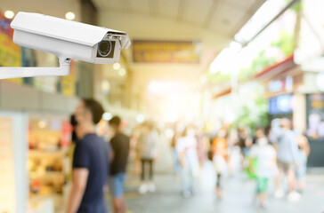 Modern public CCTV camera with blur crowd and shopping plaza background. Recording cameras for monitoring all day and night. Concept of surveillance and monitoring with copy space.