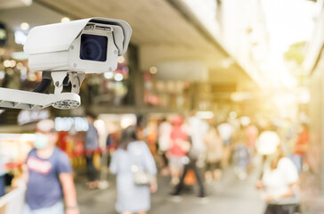Modern public CCTV camera with blur crowd and shopping plaza background. Recording cameras for monitoring all day and night. Concept of surveillance and monitoring with copy space. - obrazy, fototapety, plakaty