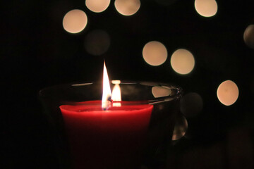 red candle flame at night with lights in background
