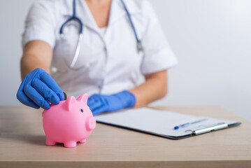 A faceless female doctor puts a coin in a piggy bank