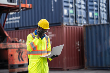 African technician dock worker in protective safety jumpsuit uniform and with hardhat and use laptop computer at cargo container shipping warehouse. transportation import,export logistic industrial
