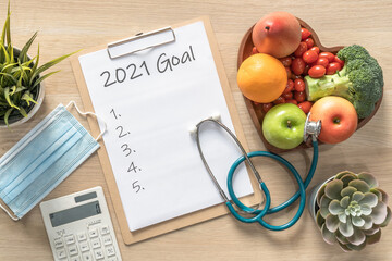 2021 New Year Goals in new normal lifestyle, work-life balance with face mask safety awareness from covid-19, healthy food, good heart health, blank resolution list on white paper medical clipboard