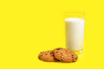 Chocolate chip cookies and a glass of milk on a bright yellow background.