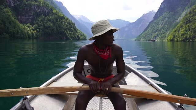 afro american man is rowing in a rowboat on the konigsee Germany