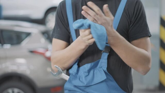 Unrecognizable auto mechanic in uniform rubbing hands with cloth indoors. Young Caucasian service man cleaning palms after work in car workshop. Industrial concept.