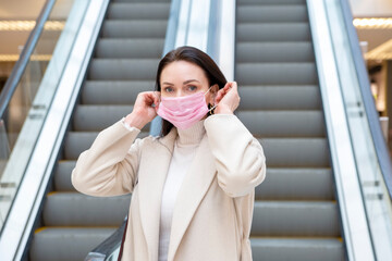 Fototapeta premium beautiful woman putting on pink medical mask on her face against the background of the escadator in a public place
