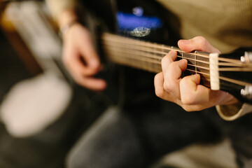 Playing acoustic guitar. The guy is playing chords on the guitar. Black guitar, fingers. Evening...
