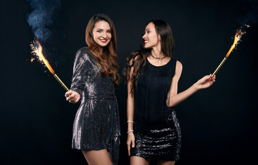 Two pretty crazy best friends in fashion dresses posing with fireworks