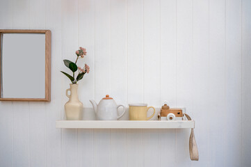 Living room interior with flower in vase, ceramic pot, cup, camera mockup and empty wooden picture frame on wooden wall