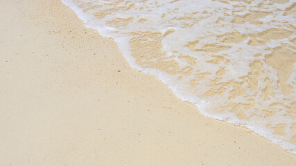 soft wave of the sea on sandy beach texture background in bright summer day