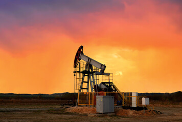 Crude oil pump jack at oilfield on atmospheric sunset backround. Fossil crude output and fuels oil...