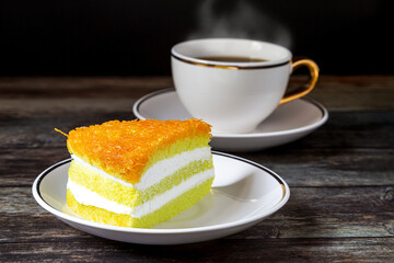 
Pandan leaf coconut cake topped with golden thread. Placed on the plate and coffee cup on the table, ready to serve.