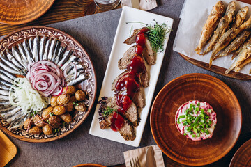 home wooden table covered with plates with various delicious dishes in the Slavic style: sourdough, salted and fried fish, potatoes, fried meat and salads
