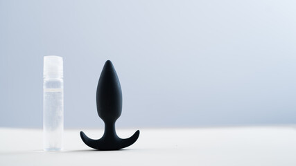 BLACK ANAL PLUG AND A BOTTLE OF LUBRICANTS ON A TABLE ON A WHITE BACKGROUND.