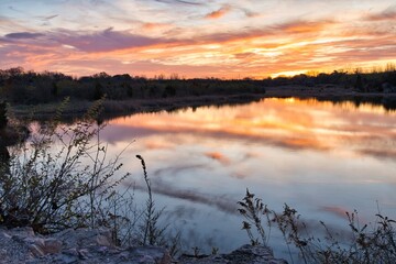 Sunrise reflecting off of quarry and lake on brisk fall morning. Amazing colors of firey sky light up the morning. Orange and red contrast with blue in sunrise or sunset