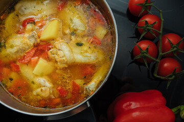 Soup with poultry, potatoes and greenery. Tomatoes and peppers next to a saucepan with soup