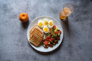 Top view of healthy food items bread slices, boiled vegetables and eggs in a plate along with condiments.