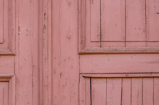 Fragment of an old wooden door painted with pink paint. A background from an old surface with cracked paint. Selective focus.