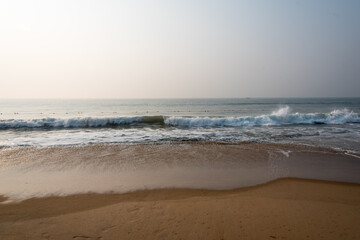 A day at the beach with waves of a calm sea splashing on the shore.