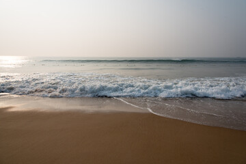 Gentle waves of a sea hitting the shore under a hazy winter sun.